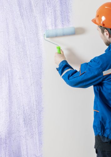 worker painter painting the wall surface with a roller, man at work decorating a room